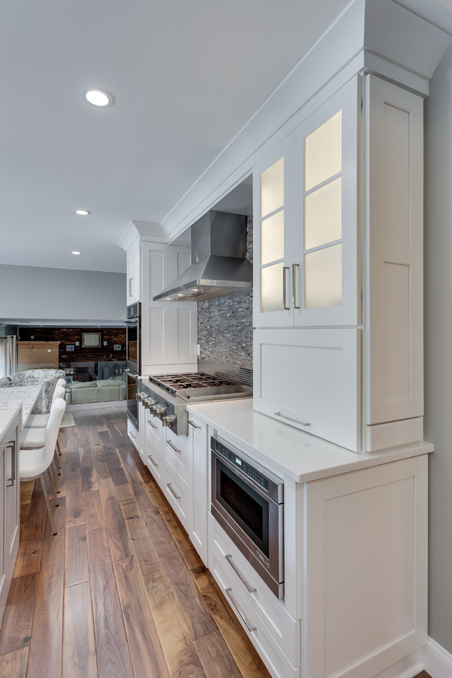 Mid-sized trendy galley medium tone wood floor eat-in kitchen photo in DC Metro with a double-bowl sink, shaker cabinets, white cabinets, quartzite countertops, gray backsplash, stone tile backsplash, stainless steel appliances and an island