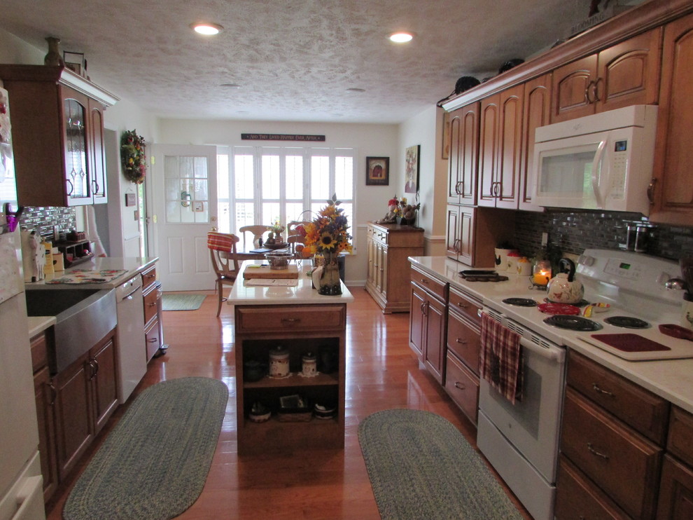 Example of a mid-sized country galley medium tone wood floor eat-in kitchen design in Other with a farmhouse sink, raised-panel cabinets, medium tone wood cabinets, quartz countertops, multicolored backsplash, slate backsplash, white appliances and an island