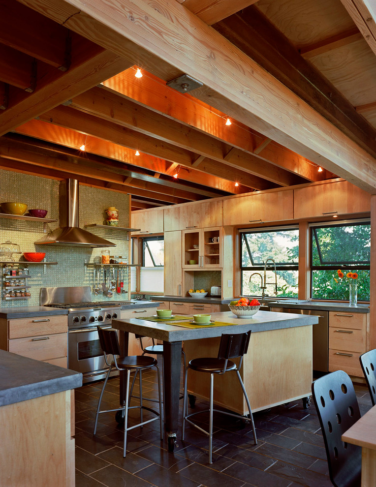 Cette image montre une cuisine américaine design en bois clair avec un placard à porte plane, une crédence verte, une crédence en mosaïque et un électroménager en acier inoxydable.