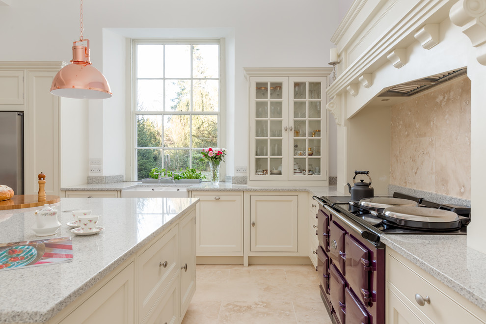 Aménagement d'une grande cuisine américaine classique en L avec un évier de ferme, un placard à porte shaker, des portes de placard blanches, un plan de travail en granite, une crédence beige, une crédence en pierre calcaire, un électroménager de couleur, un sol en calcaire, îlot, un sol beige et un plan de travail gris.