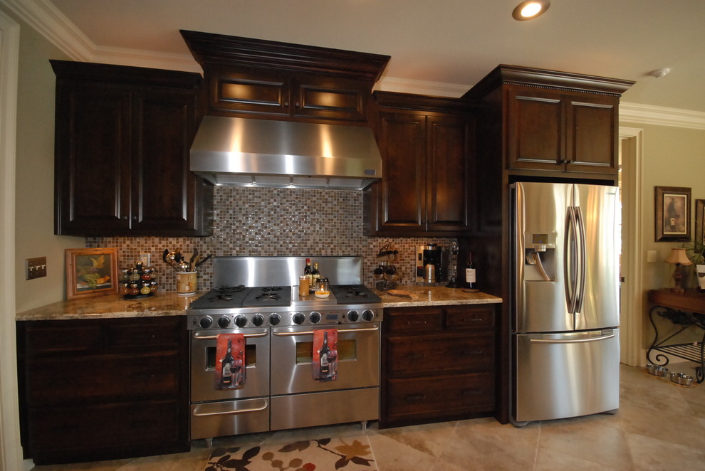 Cette image montre une cuisine linéaire traditionnelle en bois foncé avec un placard avec porte à panneau surélevé, une crédence multicolore, une crédence en mosaïque et un électroménager en acier inoxydable.