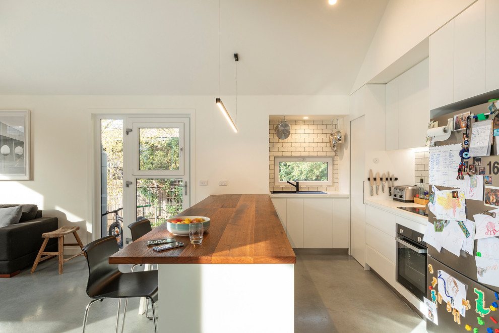 Exempel på ett litet modernt kök, med en enkel diskho, släta luckor, vita skåp, träbänkskiva, vitt stänkskydd, stänkskydd i tunnelbanekakel, rostfria vitvaror, betonggolv, en köksö och grått golv