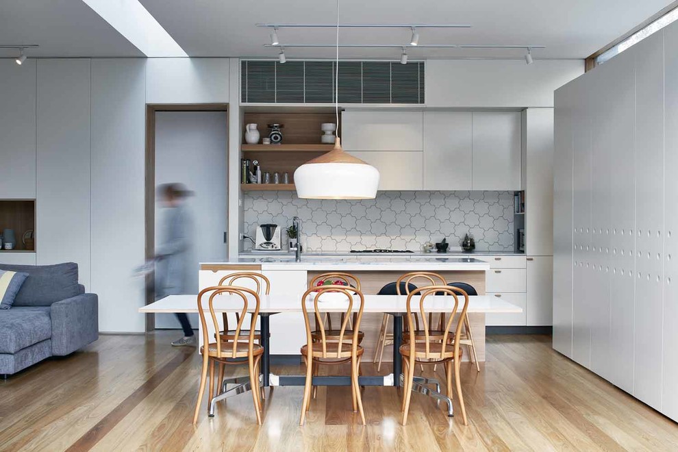 Medium sized contemporary galley open plan kitchen in Melbourne with a submerged sink, flat-panel cabinets, white cabinets, marble worktops, white splashback, mosaic tiled splashback, stainless steel appliances, light hardwood flooring, an island, beige floors and beige worktops.