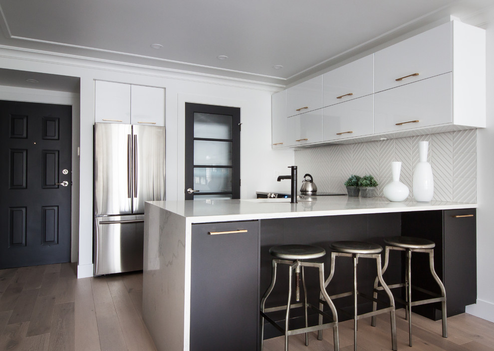 Foto på ett funkis kök, med en undermonterad diskho, släta luckor, svarta skåp, vitt stänkskydd, rostfria vitvaror, mellanmörkt trägolv, en halv köksö och brunt golv