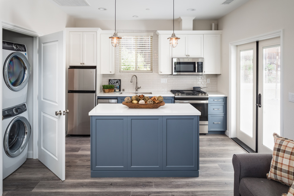 Example of a transitional galley gray floor open concept kitchen design in San Diego with an undermount sink, shaker cabinets, blue cabinets, white backsplash, stainless steel appliances, an island and white countertops