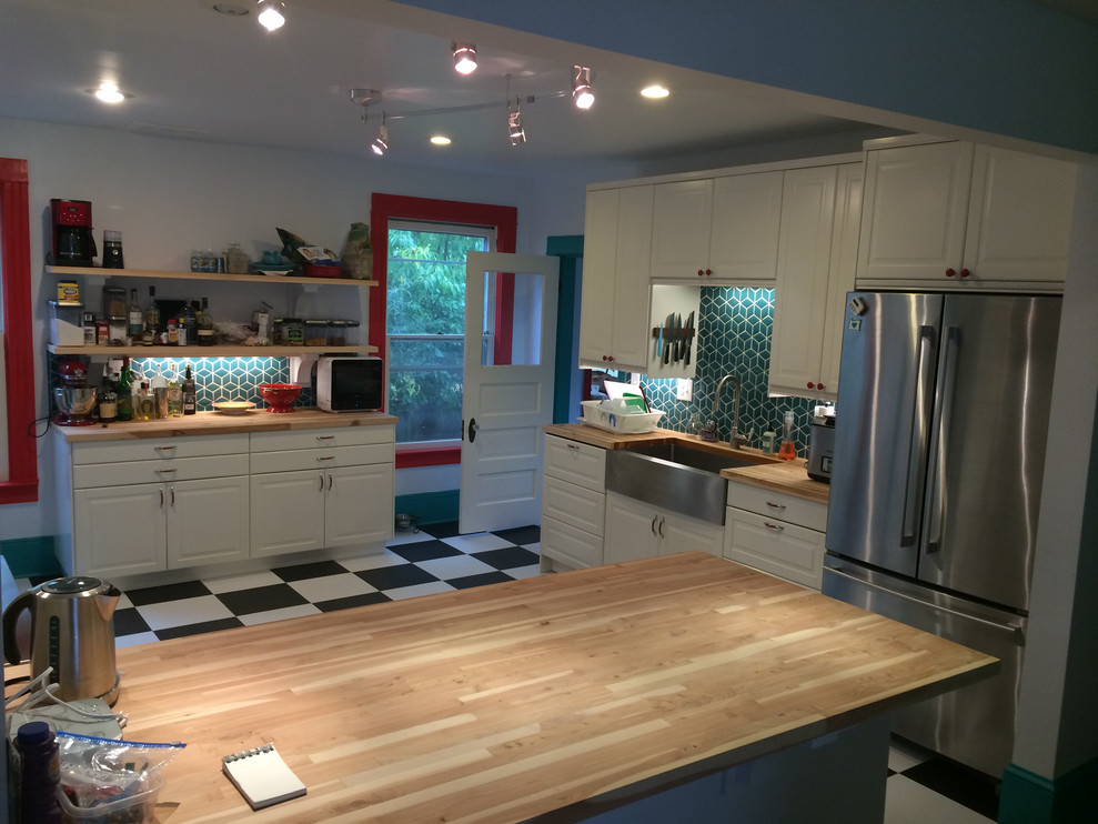 Foto på ett mellanstort funkis brun kök, med en rustik diskho, luckor med upphöjd panel, vita skåp, träbänkskiva, grönt stänkskydd, stänkskydd i keramik, rostfria vitvaror, vinylgolv, en halv köksö och svart golv