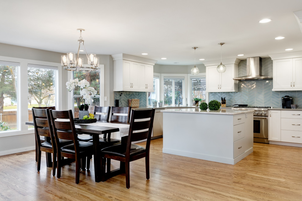 Mid-sized transitional u-shaped medium tone wood floor and brown floor eat-in kitchen photo in Boise with a single-bowl sink, shaker cabinets, white cabinets, solid surface countertops, black backsplash, ceramic backsplash, stainless steel appliances, an island and gray countertops