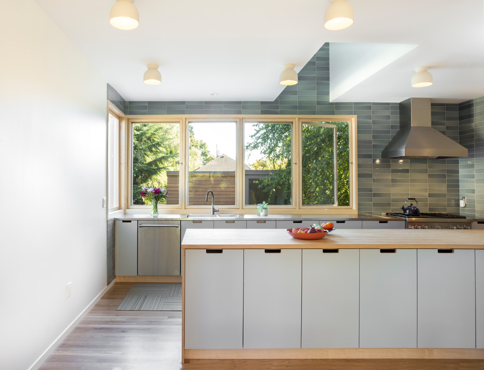 Inspiration for a 1960s galley dark wood floor and brown floor kitchen remodel in Portland with a double-bowl sink, flat-panel cabinets, gray cabinets, wood countertops, green backsplash, stainless steel appliances, a peninsula and beige countertops