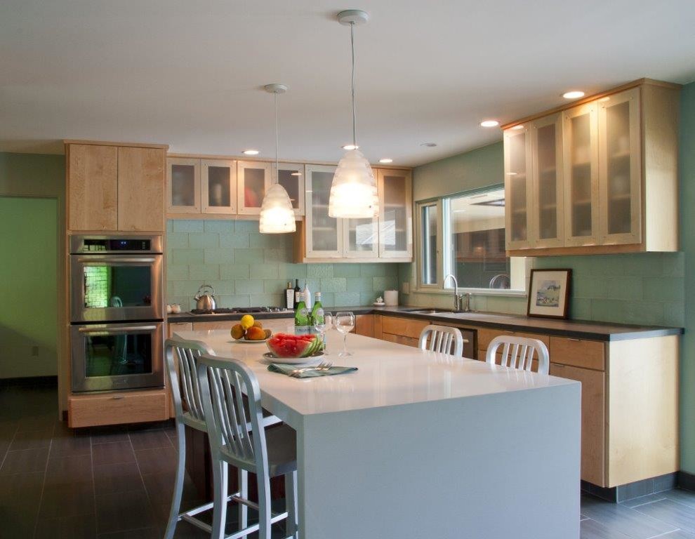 Large midcentury u-shaped enclosed kitchen in Portland with flat-panel cabinets, light wood cabinets, soapstone worktops, green splashback, glass tiled splashback, stainless steel appliances, porcelain flooring, an island, a submerged sink and grey floors.