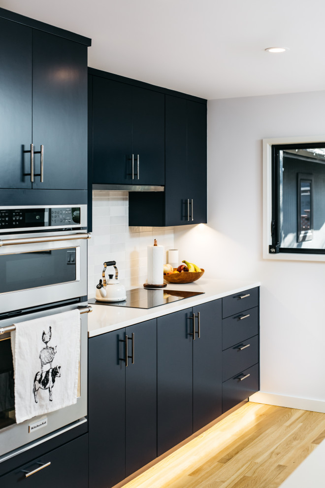 This is an example of a contemporary single-wall kitchen in Portland with flat-panel cabinets, white splashback, medium hardwood flooring, brown floors and white worktops.