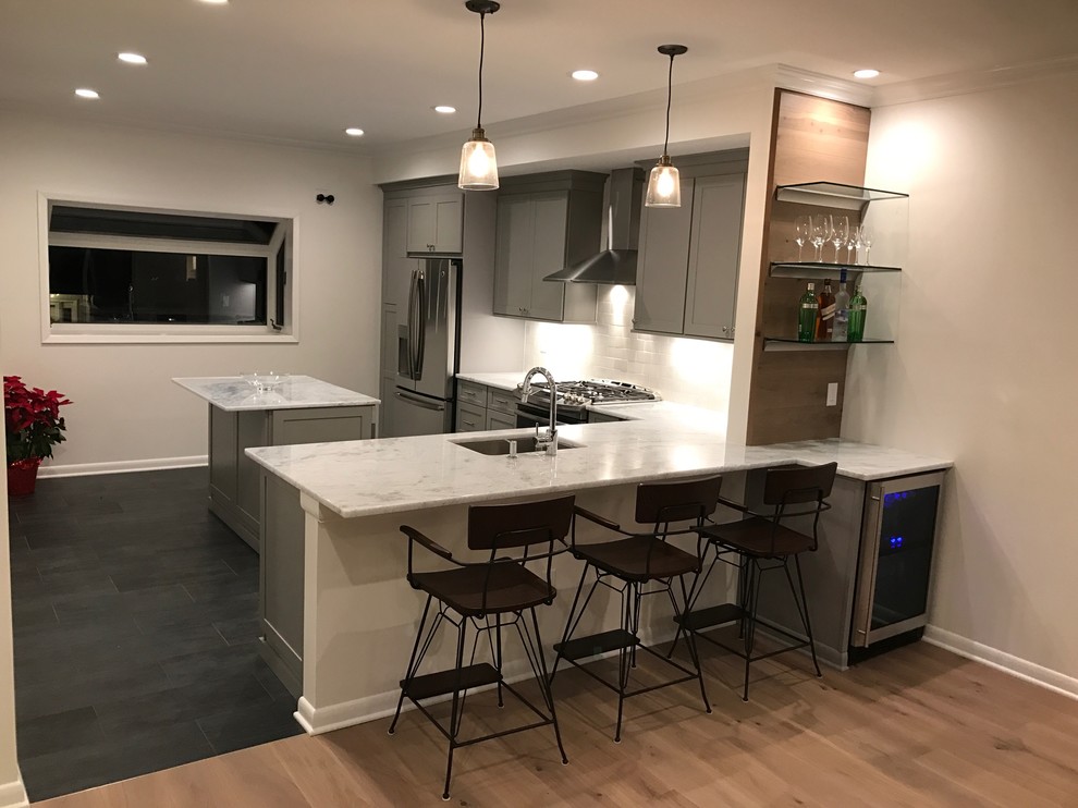 Photo of a medium sized classic l-shaped kitchen/diner in New York with a submerged sink, shaker cabinets, grey cabinets, marble worktops, white splashback, stone tiled splashback, stainless steel appliances, dark hardwood flooring and an island.