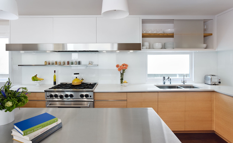 Photo of a modern kitchen in San Francisco with stainless steel appliances, a double-bowl sink, flat-panel cabinets, light wood cabinets, white splashback, glass sheet splashback and composite countertops.