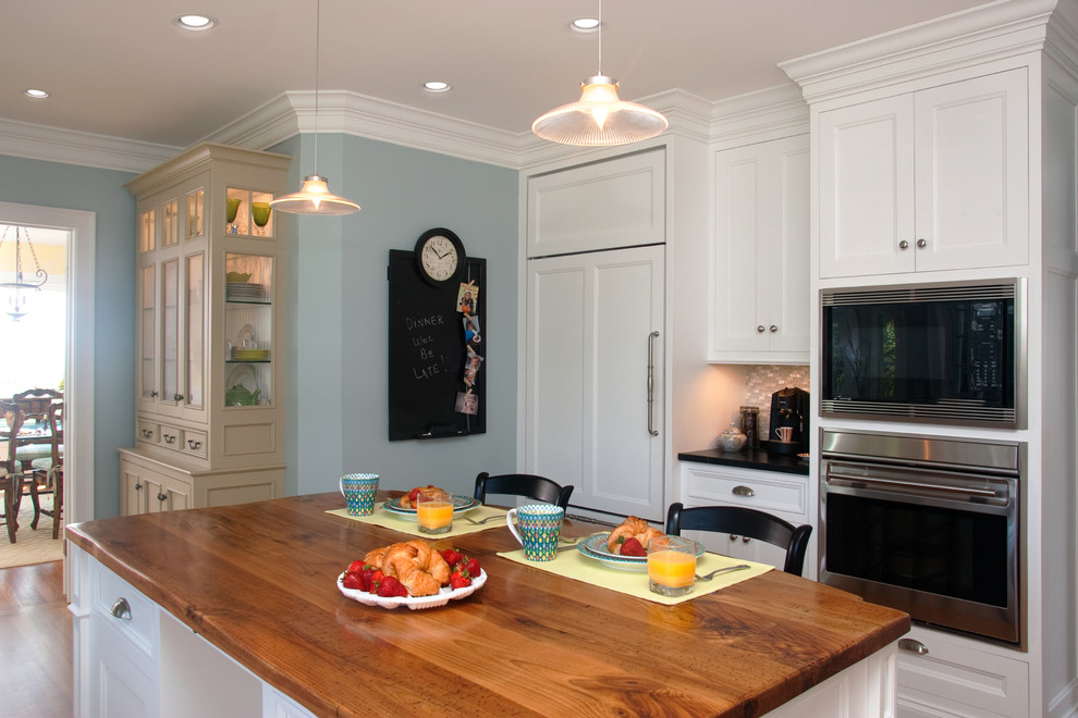 Immagine di una cucina tradizionale di medie dimensioni con lavello sottopiano, ante bianche, top in legno, paraspruzzi bianco, elettrodomestici in acciaio inossidabile e parquet chiaro