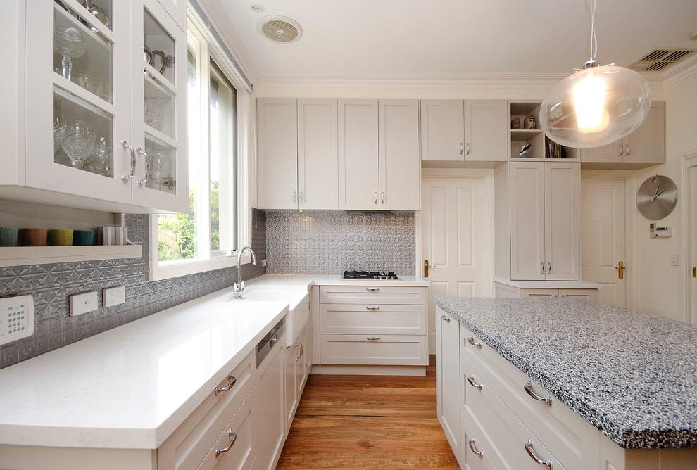 Example of a mid-sized transitional l-shaped medium tone wood floor enclosed kitchen design in Melbourne with an island, a farmhouse sink, shaker cabinets, beige cabinets, quartz countertops, gray backsplash, metal backsplash and stainless steel appliances