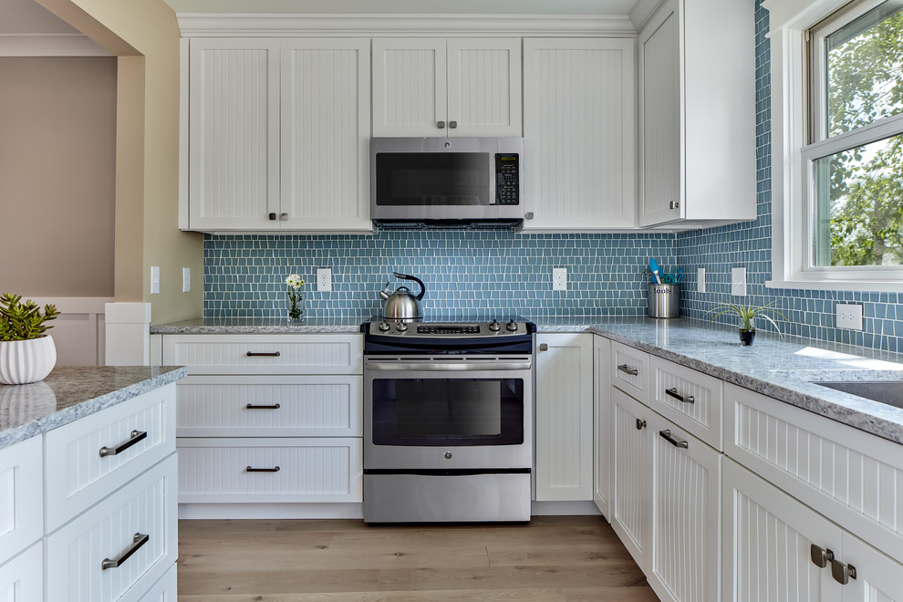 Foto på ett mellanstort amerikanskt kök, med en undermonterad diskho, vita skåp, bänkskiva i kvarts, blått stänkskydd, stänkskydd i mosaik, rostfria vitvaror, ljust trägolv, beiget golv, skåp i shakerstil och en köksö