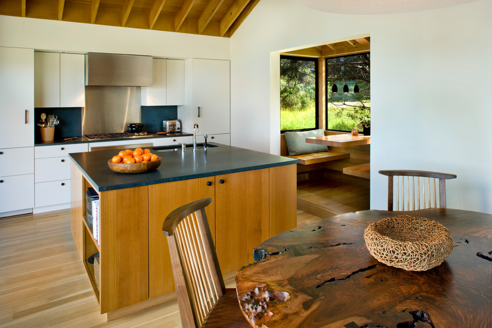 Foto på ett rustikt kök och matrum, med en undermonterad diskho, släta luckor, vita skåp, stänkskydd med metallisk yta, ljust trägolv och en köksö