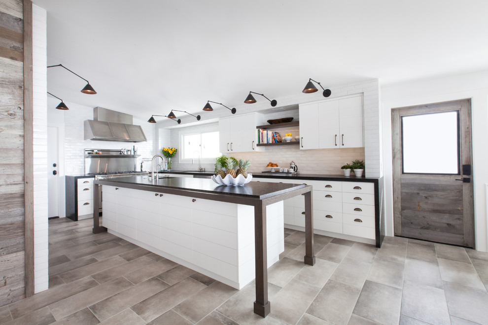 Foto på ett mellanstort funkis kök, med en undermonterad diskho, vita skåp, vitt stänkskydd, rostfria vitvaror, en köksö, granitbänkskiva, stänkskydd i tegel, klinkergolv i porslin, beiget golv och släta luckor