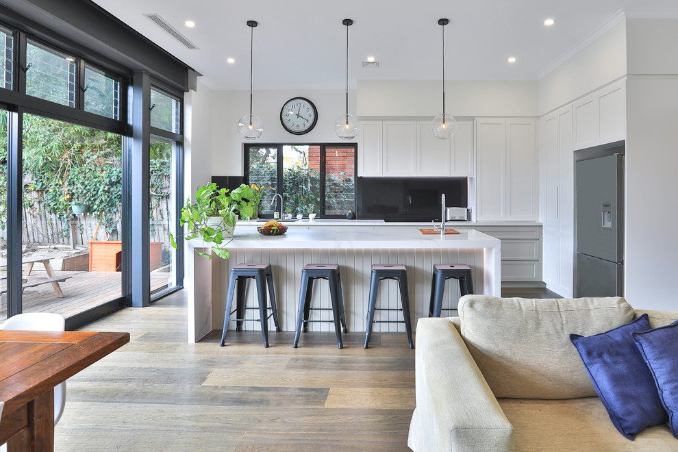 Bild på ett stort funkis flerfärgad flerfärgat kök, med en undermonterad diskho, skåp i shakerstil, vita skåp, bänkskiva i kvarts, svart stänkskydd, stänkskydd i marmor, rostfria vitvaror, mellanmörkt trägolv, en köksö och brunt golv