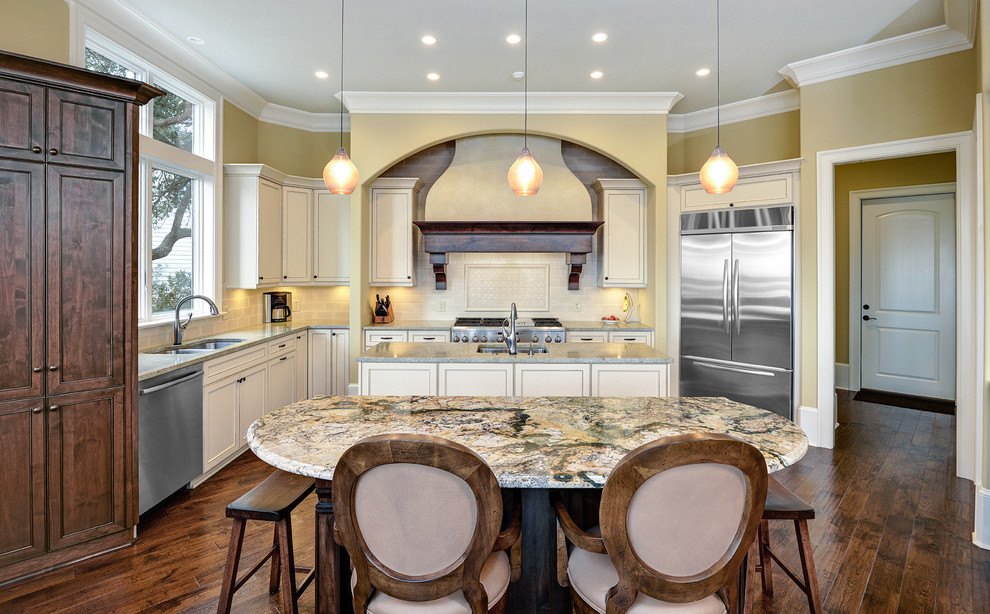 Klassisk inredning av ett stort flerfärgad flerfärgat kök, med stänkskydd i keramik, en undermonterad diskho, luckor med infälld panel, vita skåp, bänkskiva i kvartsit, vitt stänkskydd, rostfria vitvaror, mörkt trägolv, flera köksöar och brunt golv