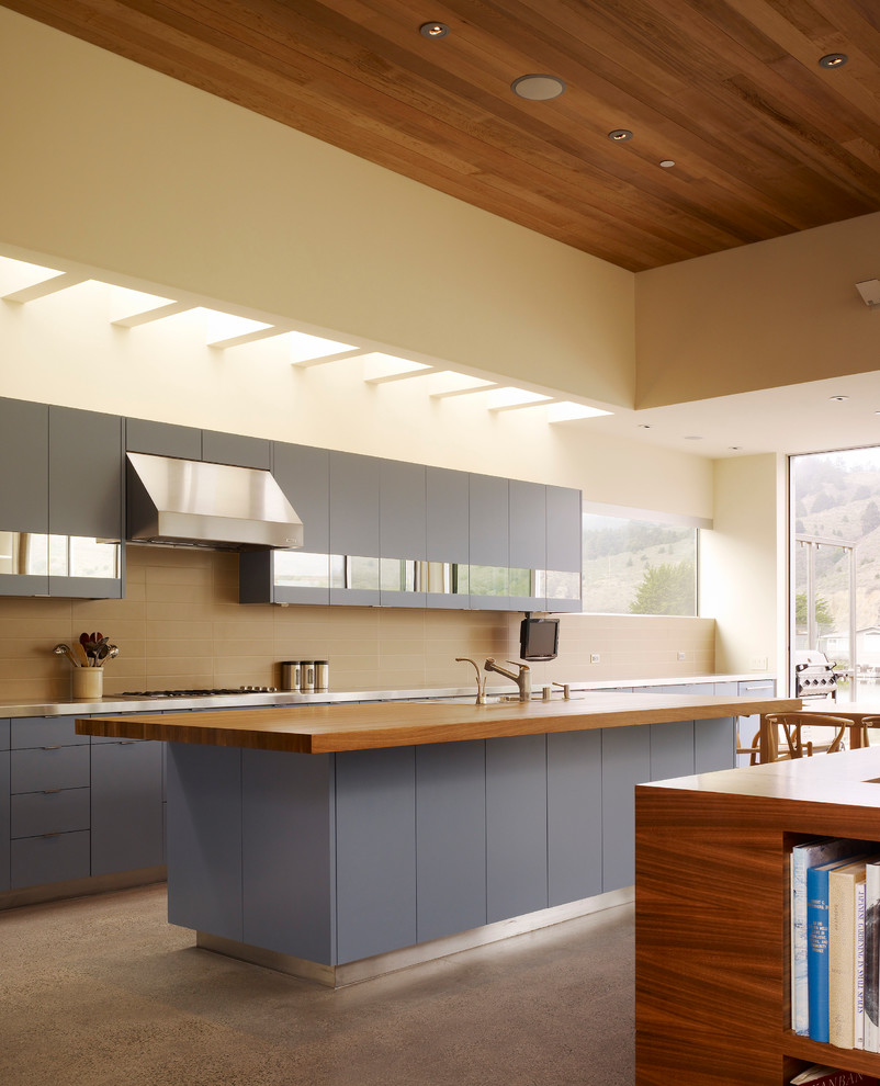 Design ideas for a medium sized beach style galley kitchen/diner in San Francisco with flat-panel cabinets, blue cabinets, brown splashback, an island, a built-in sink, stainless steel worktops and ceramic splashback.