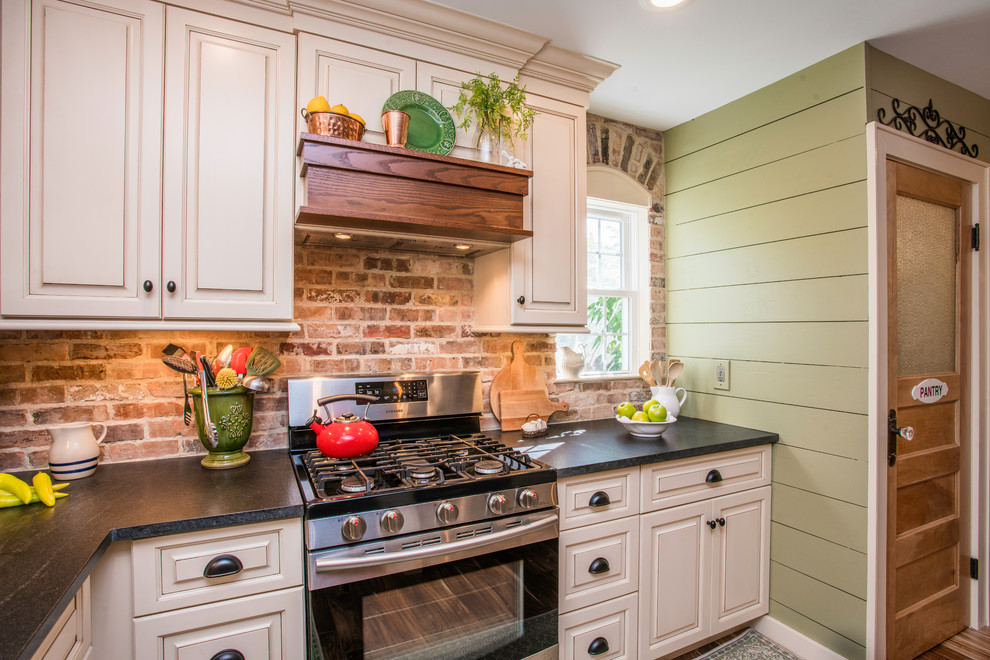 Example of a mid-sized farmhouse l-shaped dark wood floor and brown floor eat-in kitchen design in New York with a farmhouse sink, raised-panel cabinets, beige cabinets, granite countertops, brown backsplash, brick backsplash, stainless steel appliances and an island