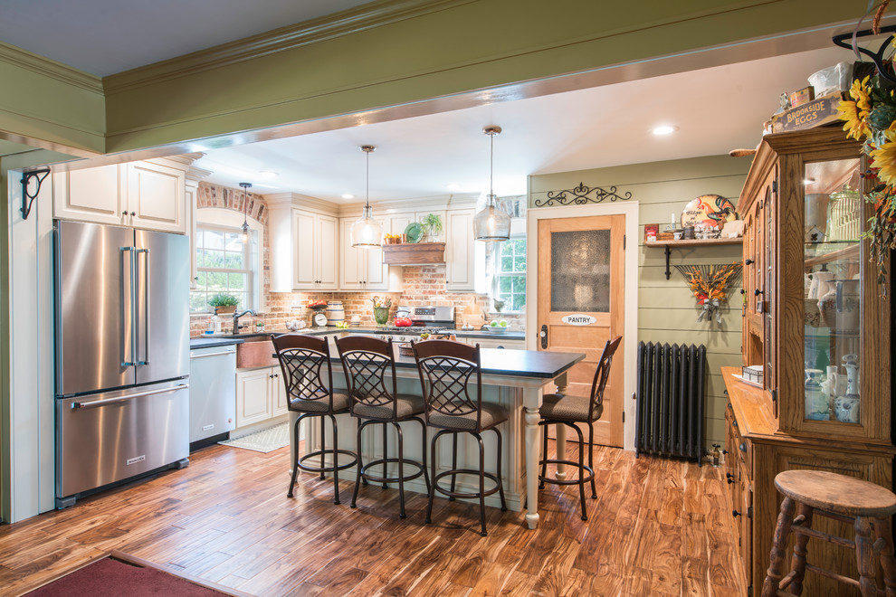 Mid-sized country l-shaped dark wood floor and brown floor eat-in kitchen photo in New York with a farmhouse sink, raised-panel cabinets, beige cabinets, granite countertops, brown backsplash, brick backsplash, stainless steel appliances and an island