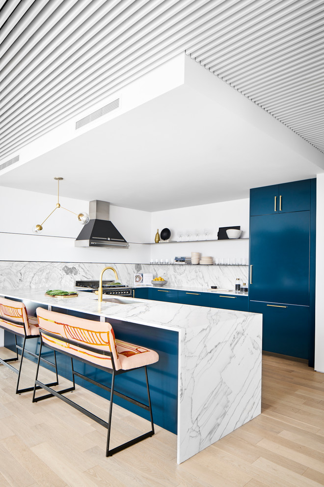 На фото: п-образная кухня в современном стиле с одинарной мойкой, плоскими фасадами, синими фасадами, серым фартуком, техникой под мебельный фасад, светлым паркетным полом, полуостровом, бежевым полом и красивой плиткой