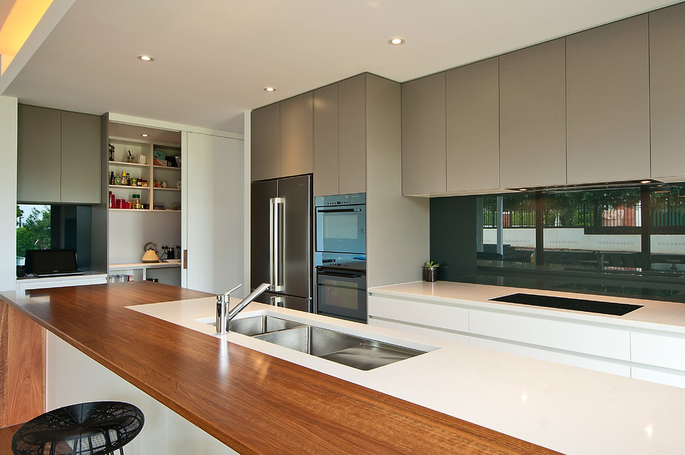 Foto på ett mycket stort funkis kök, med en undermonterad diskho, grå skåp, träbänkskiva, grått stänkskydd, glaspanel som stänkskydd, rostfria vitvaror och mellanmörkt trägolv