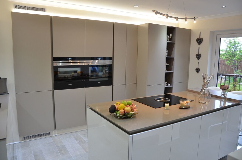 Photo of a medium sized contemporary galley kitchen/diner in Other with an integrated sink, recessed-panel cabinets, grey cabinets, integrated appliances, an island, granite worktops, white splashback, brick splashback, light hardwood flooring and grey floors.