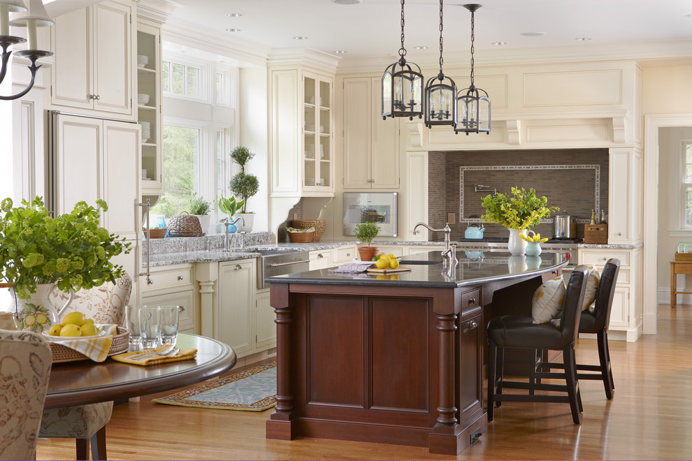 Inspiration for a large timeless l-shaped medium tone wood floor and brown floor eat-in kitchen remodel in Boston with recessed-panel cabinets, white cabinets, paneled appliances, a farmhouse sink, marble countertops, brown backsplash, mosaic tile backsplash and an island
