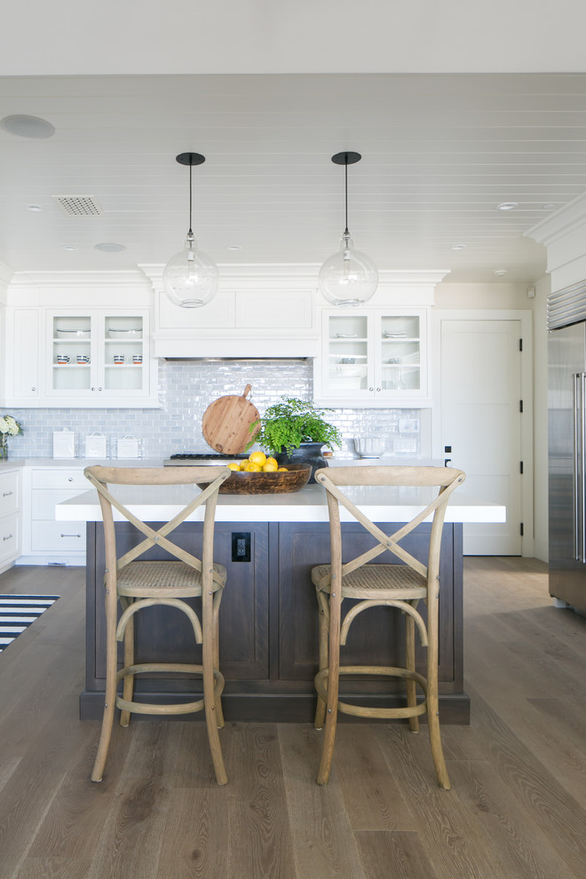 This is an example of a medium sized nautical u-shaped open plan kitchen in Orange County with a belfast sink, shaker cabinets, white cabinets, engineered stone countertops, blue splashback, ceramic splashback, stainless steel appliances, light hardwood flooring and an island.