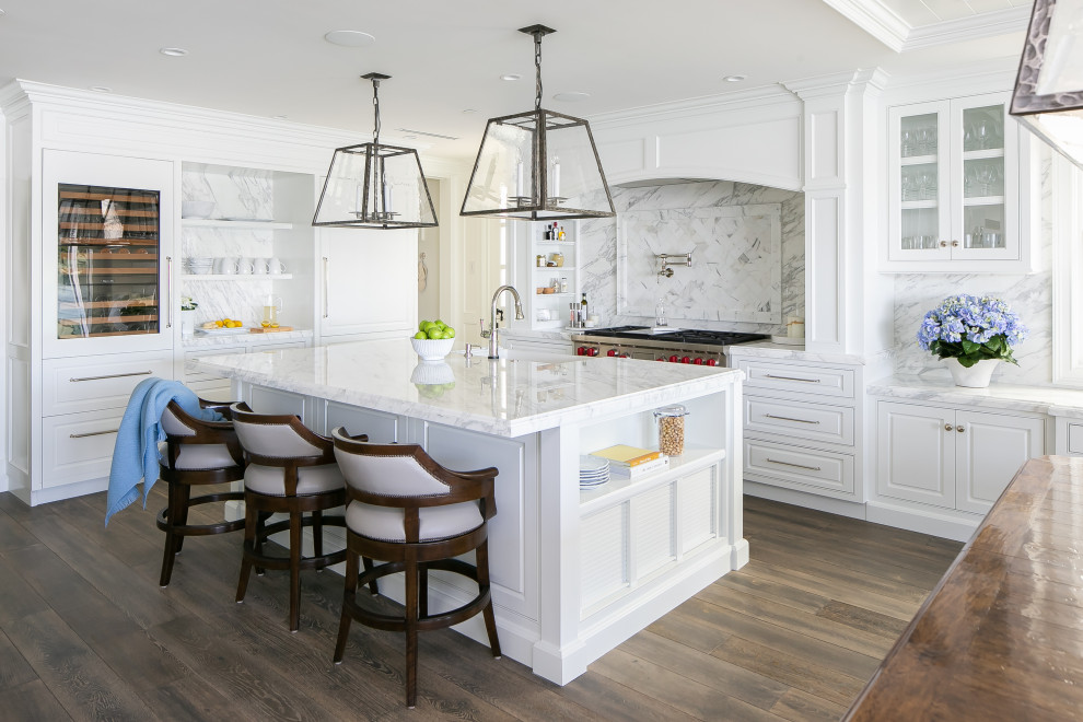 Photo of a nautical l-shaped kitchen in Orange County with a belfast sink, beaded cabinets, white cabinets, white splashback, stainless steel appliances, dark hardwood flooring, an island, brown floors and white worktops.