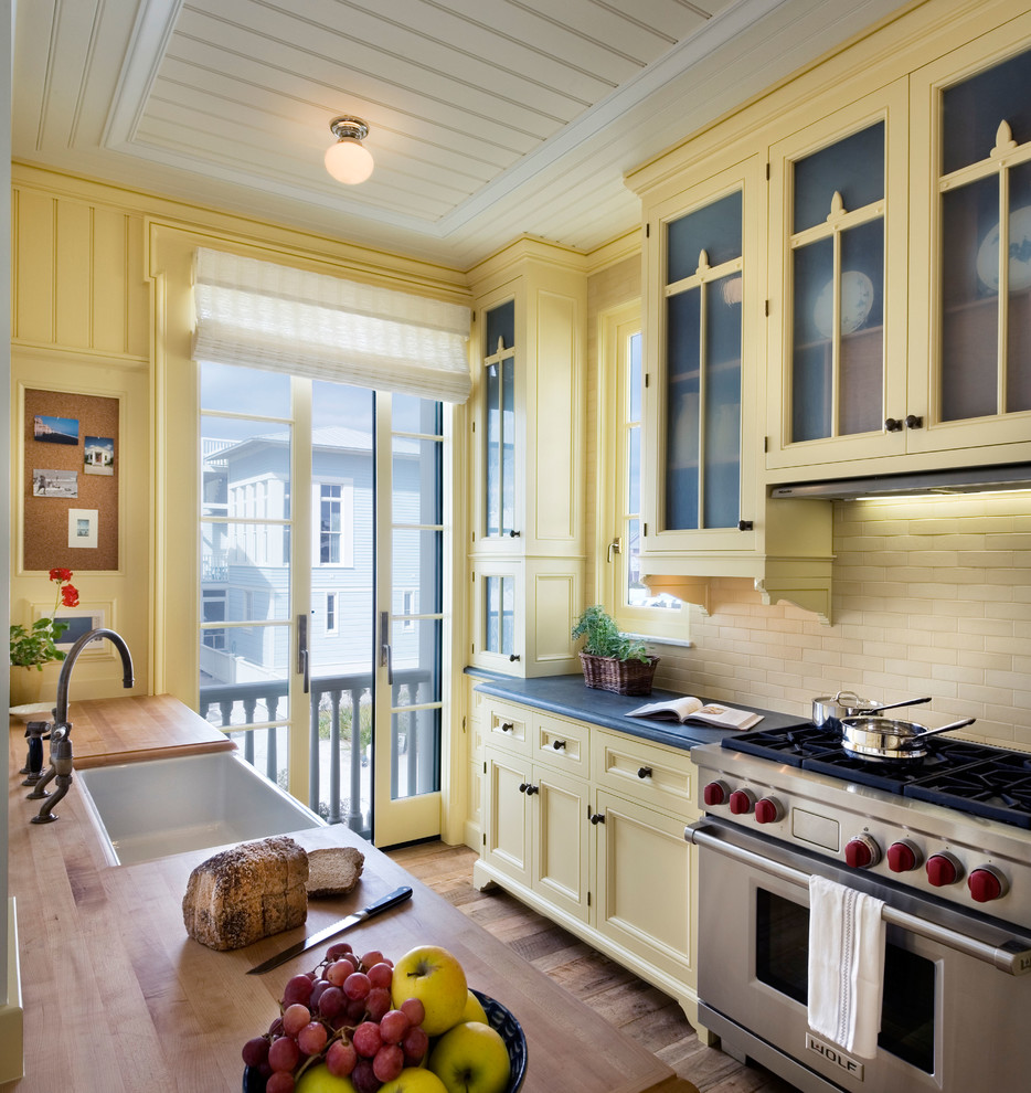 Zweizeilige Maritime Küche mit Landhausspüle, Schrankfronten mit vertiefter Füllung, gelben Schränken, Arbeitsplatte aus Holz, Küchenrückwand in Beige, Küchengeräten aus Edelstahl und braunem Holzboden in New York