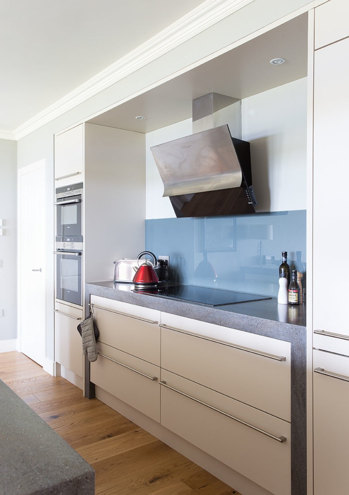 Idee per una cucina contemporanea con ante lisce, ante bianche, paraspruzzi blu, paraspruzzi con lastra di vetro e pavimento in legno massello medio