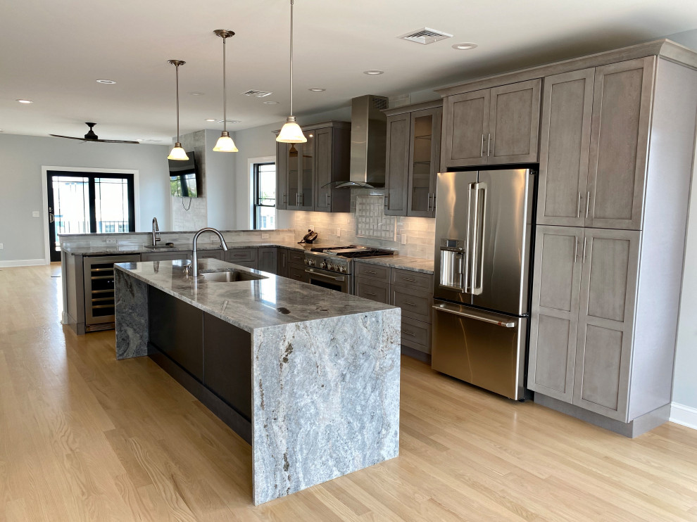 Inspiration for a mid-sized coastal l-shaped light wood floor and white floor open concept kitchen remodel in New York with an undermount sink, shaker cabinets, gray cabinets, granite countertops, gray backsplash, glass tile backsplash, stainless steel appliances, an island and gray countertops