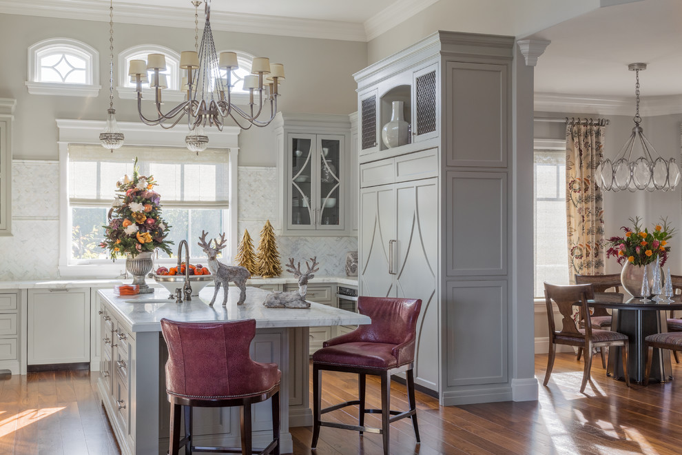 This is an example of a medium sized traditional u-shaped kitchen/diner in San Francisco with glass-front cabinets, grey cabinets, white splashback, integrated appliances, medium hardwood flooring, an island, white worktops, a belfast sink, ceramic splashback and brown floors.