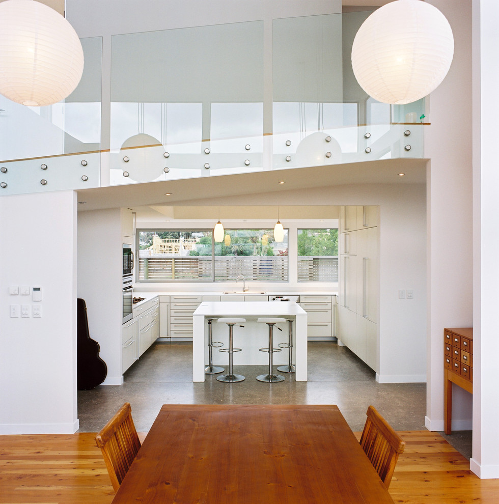 Foto på ett funkis kök och matrum, med en enkel diskho, vita skåp, laminatbänkskiva, blått stänkskydd, glaspanel som stänkskydd, rostfria vitvaror, betonggolv och en köksö
