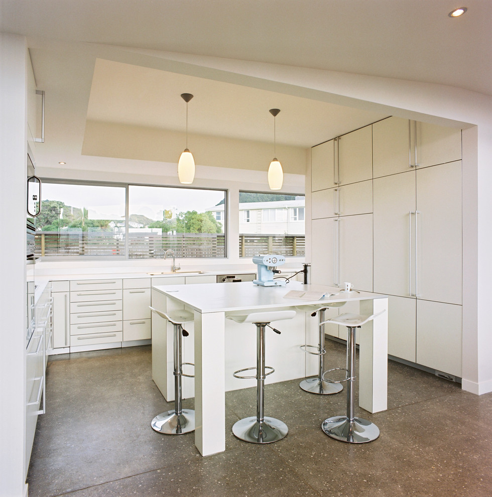 Foto di una piccola cucina design con lavello sottopiano, ante bianche, top in laminato, elettrodomestici da incasso, pavimento in cemento e ante lisce