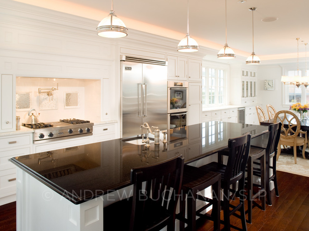Large traditional single-wall kitchen/diner in Seattle with beaded cabinets, white cabinets, granite worktops, white splashback, ceramic splashback, stainless steel appliances, dark hardwood flooring and an island.