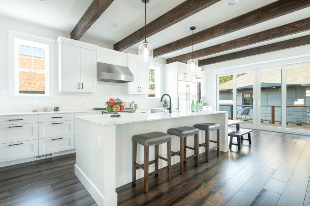 Bild på ett stort amerikanskt vit vitt kök, med en rustik diskho, skåp i shakerstil, vita skåp, bänkskiva i kvarts, vitt stänkskydd, stänkskydd i keramik, rostfria vitvaror, mellanmörkt trägolv, en köksö och flerfärgat golv