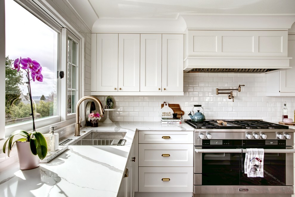 Example of a large farmhouse medium tone wood floor and brown floor kitchen design in Seattle with an undermount sink, recessed-panel cabinets, white cabinets, quartzite countertops, white backsplash, subway tile backsplash, stainless steel appliances and an island
