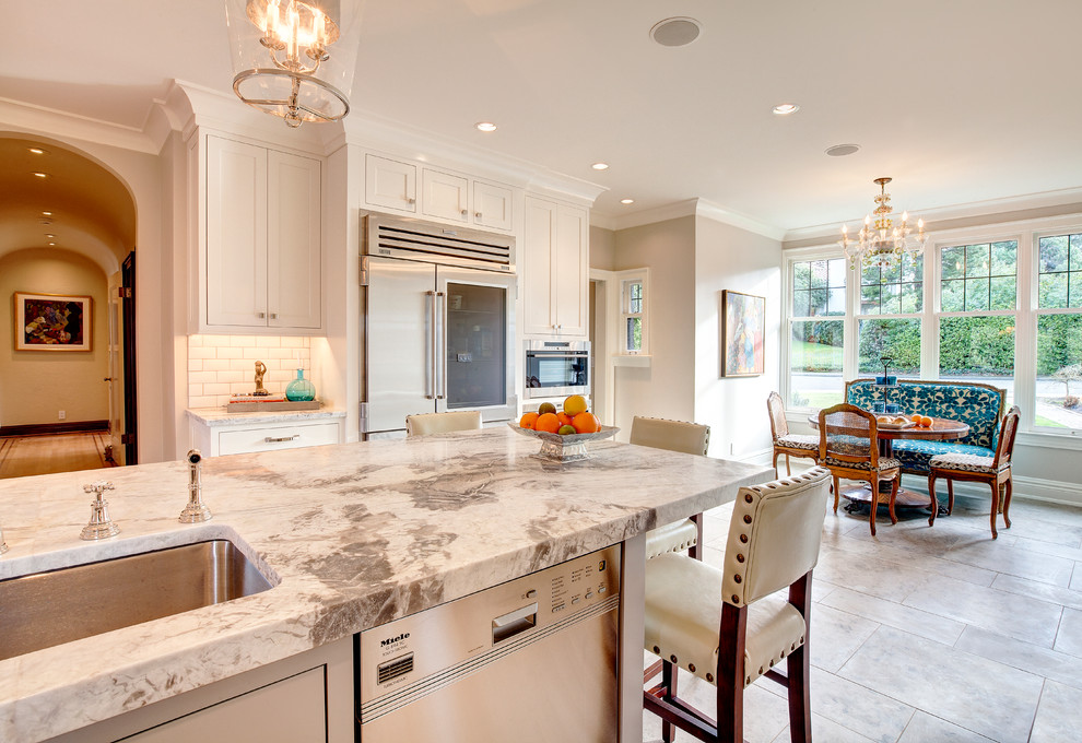 Eat-in kitchen - large transitional u-shaped porcelain tile and beige floor eat-in kitchen idea in Phoenix with an undermount sink, recessed-panel cabinets, white cabinets, granite countertops, white backsplash, ceramic backsplash, stainless steel appliances and an island