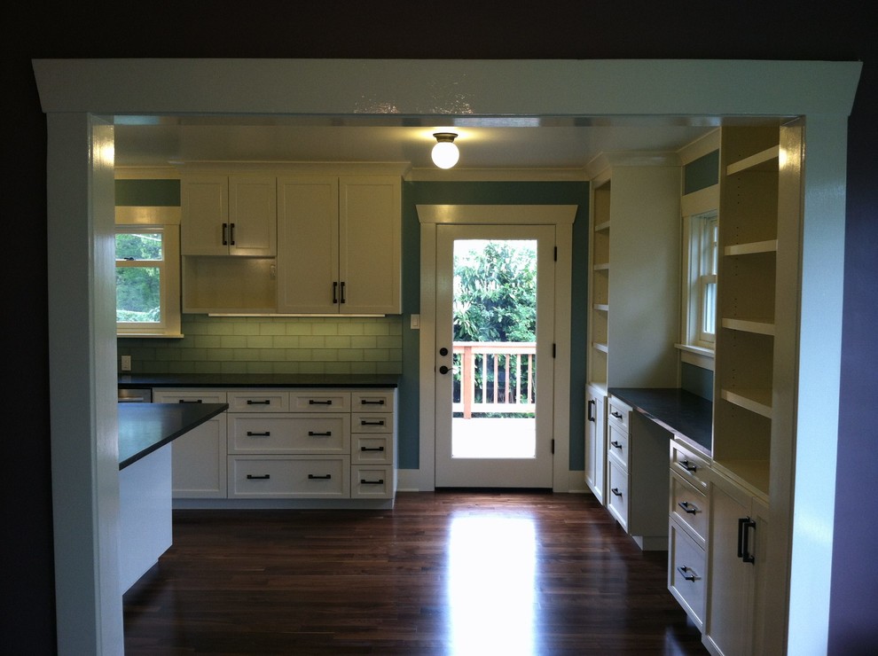 Example of a large country l-shaped dark wood floor open concept kitchen design in Seattle with a farmhouse sink, shaker cabinets, white cabinets, soapstone countertops, green backsplash, subway tile backsplash, stainless steel appliances and an island