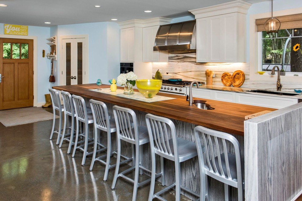 Inspiration for a large coastal single-wall concrete floor open concept kitchen remodel in Portland Maine with an undermount sink, shaker cabinets, white cabinets, wood countertops, white backsplash, stone slab backsplash, stainless steel appliances and an island