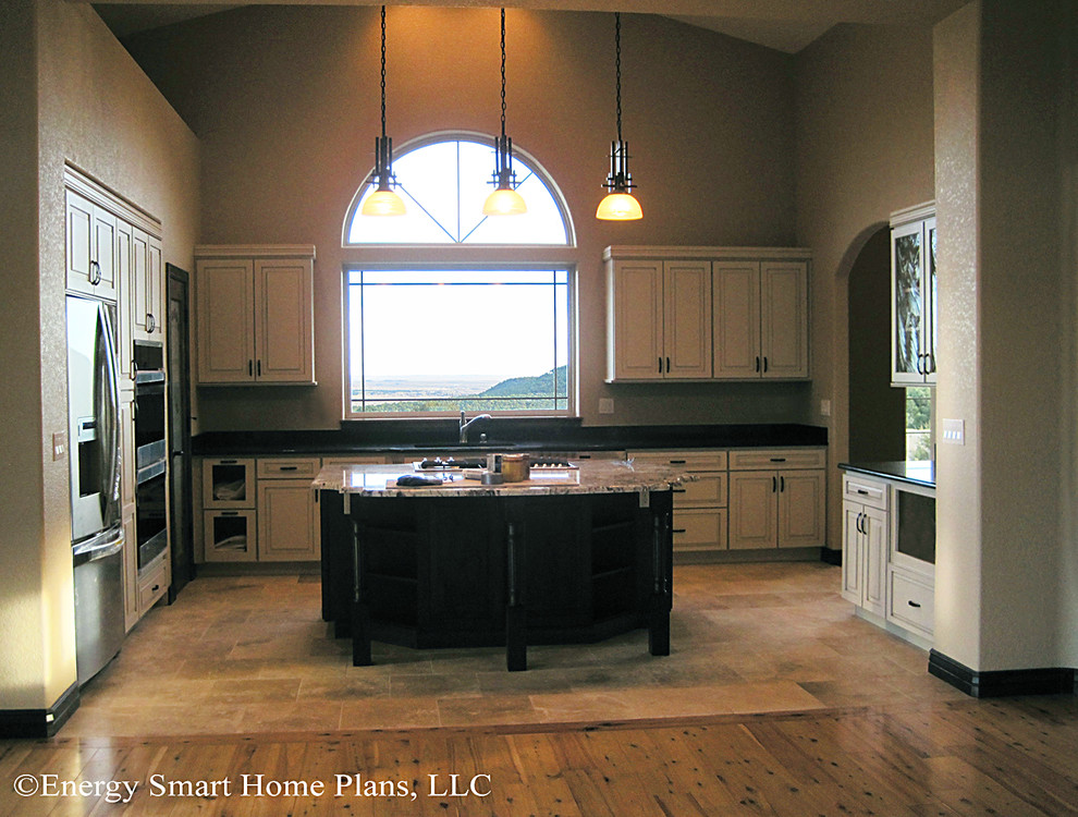 Amerikansk inredning av ett stort kök, med en undermonterad diskho, luckor med upphöjd panel, vita skåp, granitbänkskiva, rostfria vitvaror, travertin golv och en köksö