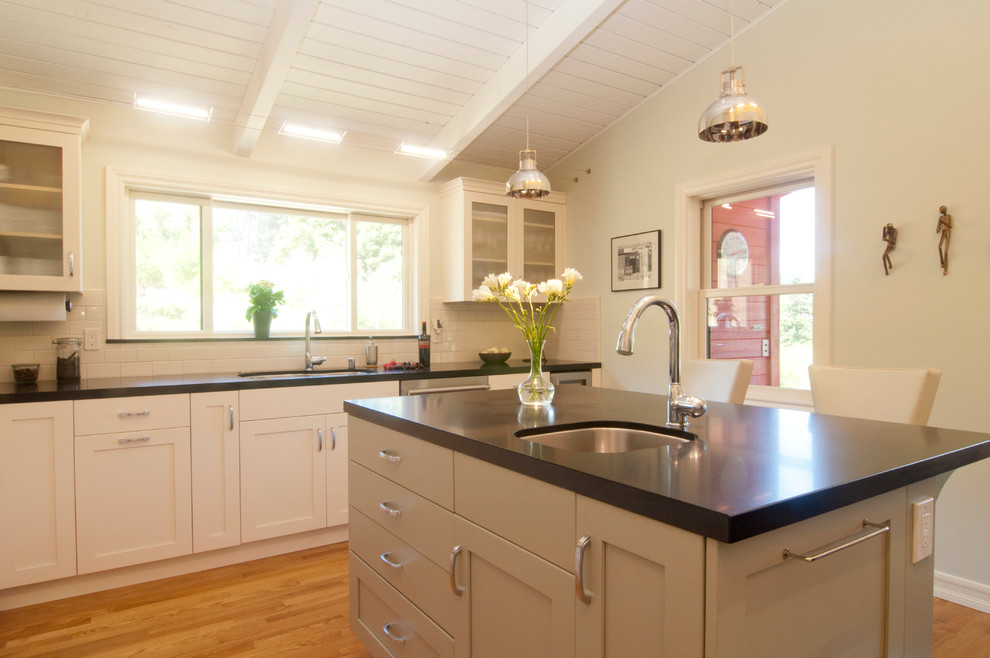 Bild på ett avskilt vintage u-kök, med en undermonterad diskho, luckor med infälld panel, vita skåp, granitbänkskiva, vitt stänkskydd, stänkskydd i keramik, rostfria vitvaror, ljust trägolv och en köksö