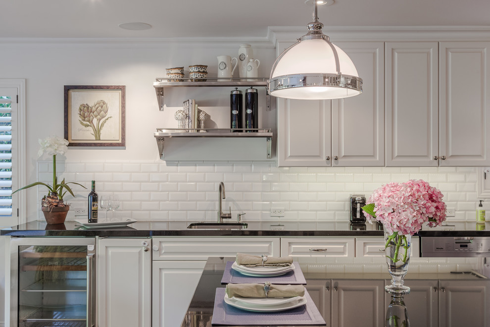 Traditional kitchen in Los Angeles with a submerged sink, raised-panel cabinets, white cabinets, white splashback, metro tiled splashback, stainless steel appliances and an island.