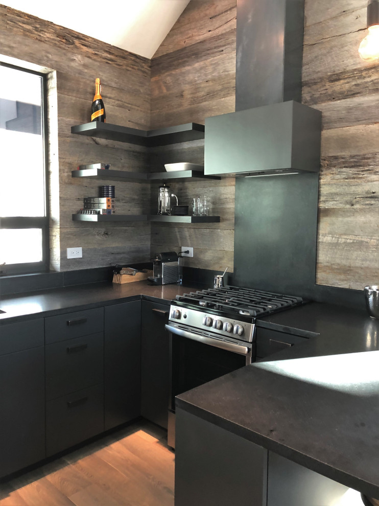 Mid-sized trendy u-shaped light wood floor, orange floor and vaulted ceiling open concept kitchen photo in Other with an undermount sink, flat-panel cabinets, black cabinets, brown backsplash, stainless steel appliances, a peninsula and brown countertops