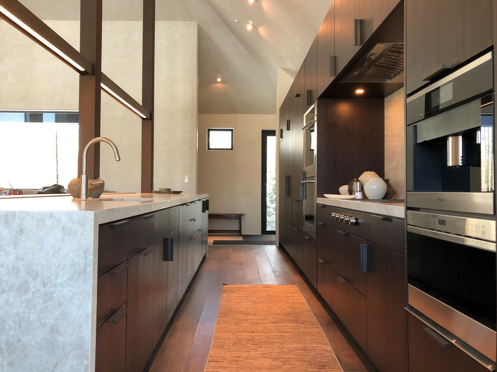 Example of a large trendy galley medium tone wood floor, brown floor and vaulted ceiling open concept kitchen design in Other with an undermount sink, flat-panel cabinets, dark wood cabinets, colored appliances, an island and multicolored countertops