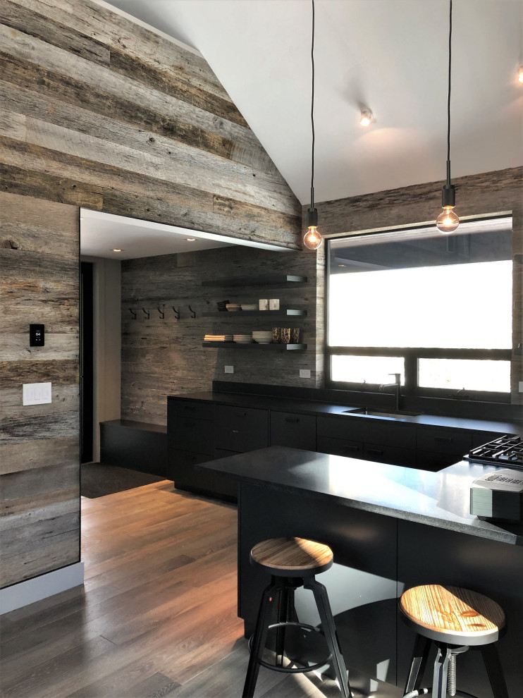 Mid-sized trendy u-shaped light wood floor, orange floor and vaulted ceiling open concept kitchen photo in Other with an undermount sink, flat-panel cabinets, black cabinets, brown backsplash, stainless steel appliances, a peninsula and brown countertops